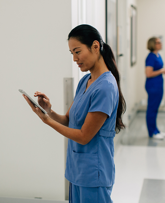 A nurse looking at a tablet in a hospital hallway.
