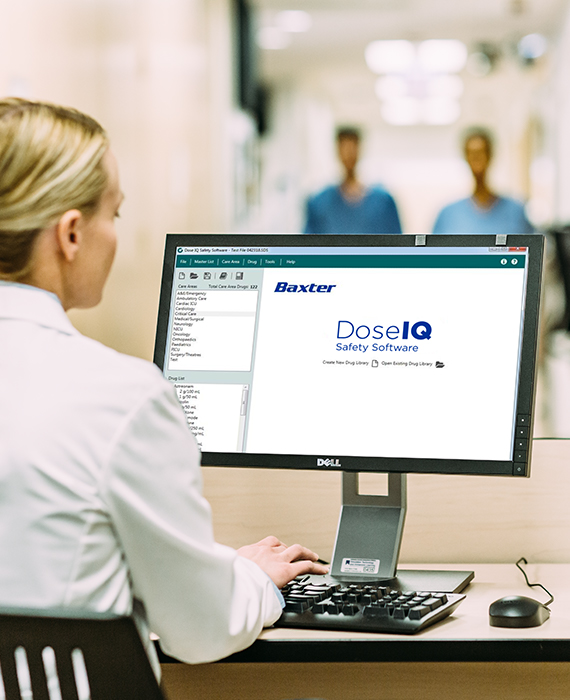 A doctor sits at a desk in a hospital looking at Dose IQ software on a computer screen. 