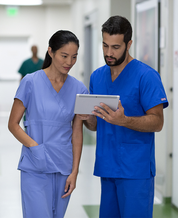 Two nurses looking at a tablet in a hospital hallway.
