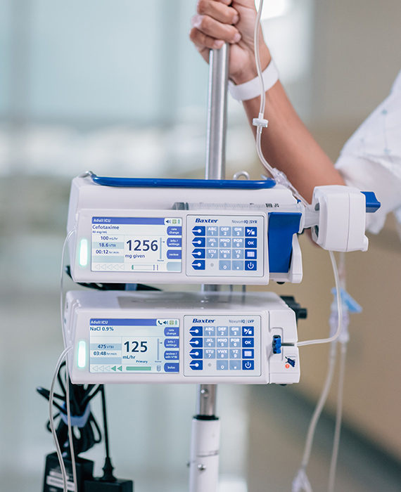 Two Novum IQ Infusion Pumps on a pole. A patient is walking down the hallway with their hand on the pole.