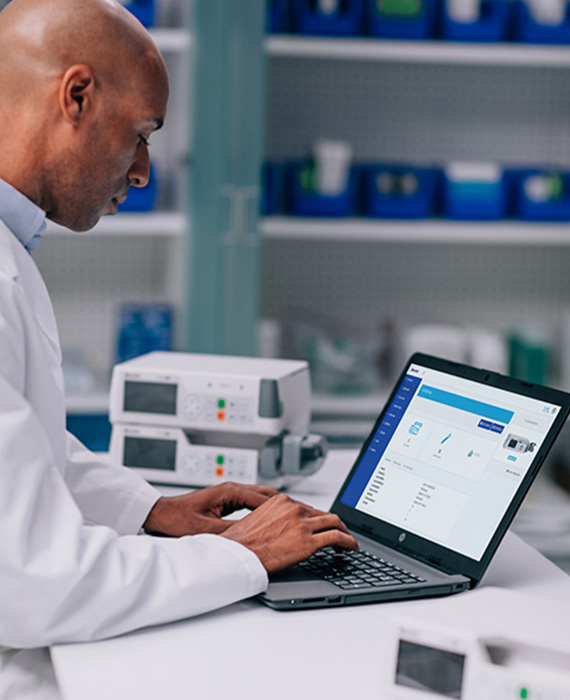 A pharmacist entering data into a computer. He has several EVO IQ pumps on the desk.