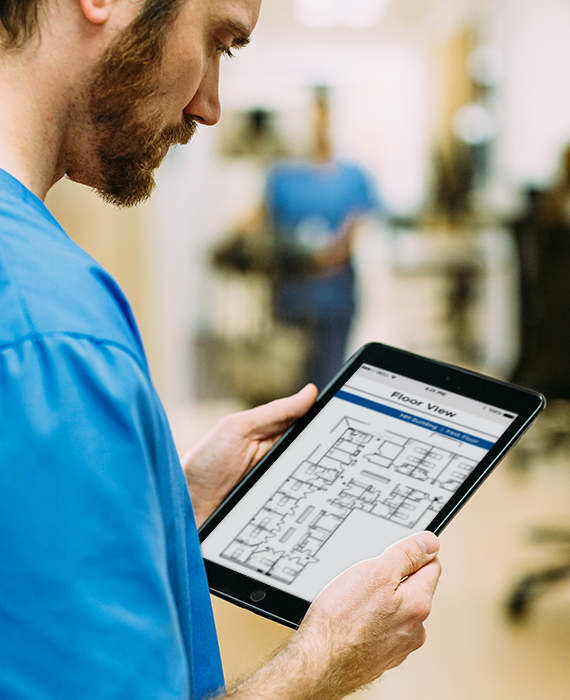 A male nurse looking at a tablet in a hospital environment.