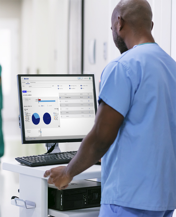 Nurse with a tablet looking at analytics while at a patients beside. An older gentleman is in the hospital bed.